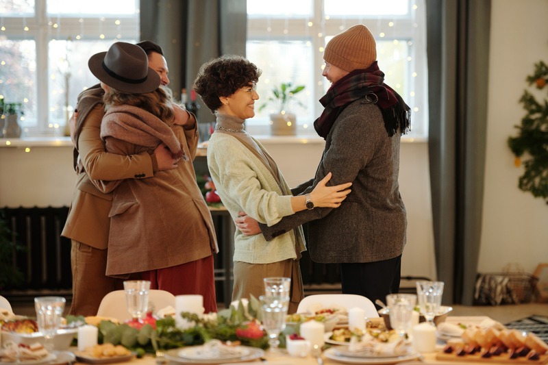 Four people greeting each other with food on a table and holiday decorations
