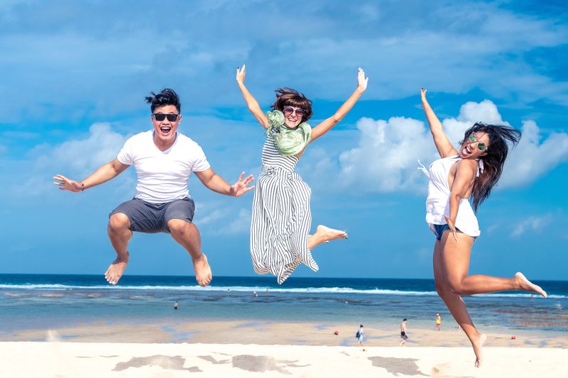 Three people on a beach jumping in the air with arms outstretched, looking happy