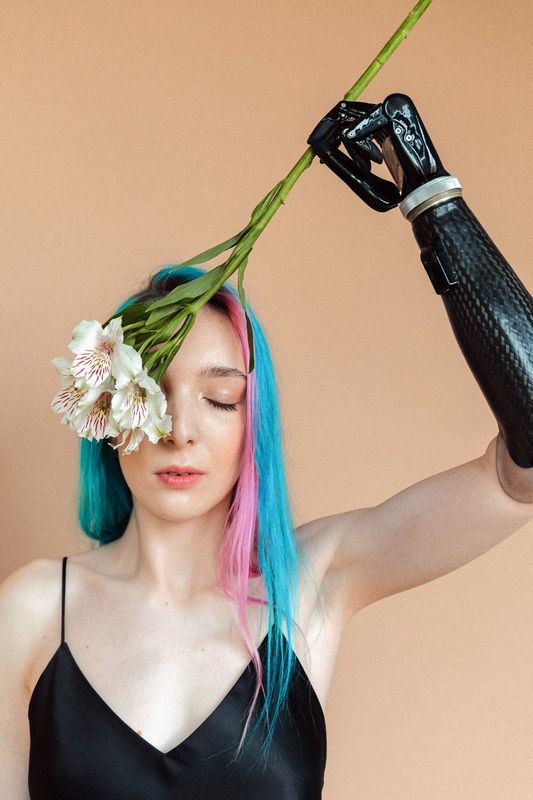 Person with blue and pink hair and a prosthetic arm holding a flower