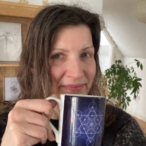 alt="Picture of Esther drinking a cup of tea out of a mug with Metatron's Cube on it (her design)"